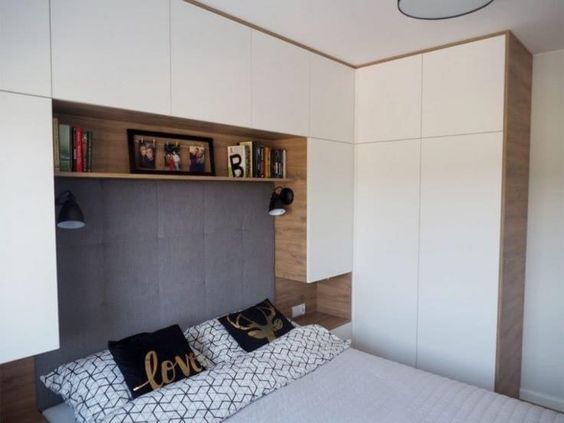 В современной спальной комнате шкаф не является самостоятельным элементом, а делается комплексная меблировка, которая включает застройку пространства над кроватной спинкой
